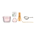 Set of tea-making tools including a pink glass, container, whisk, and other accessories on a white background.