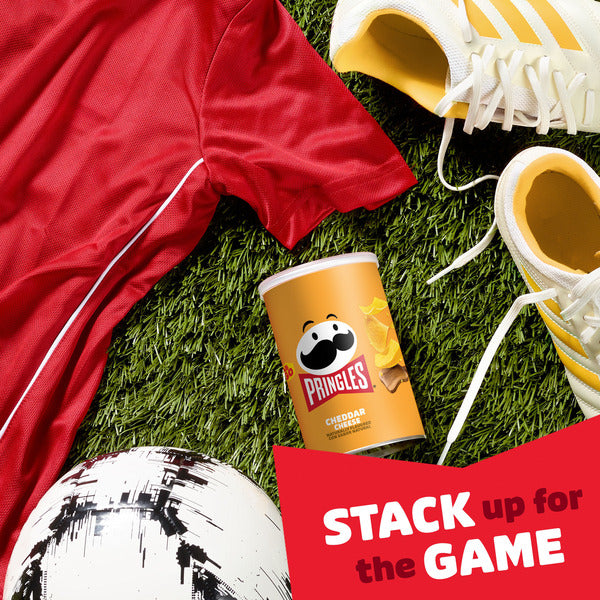 Pringles can with a soccer ball, red jersey, and yellow sneakers on grass with 'Stack up for the Game' text.