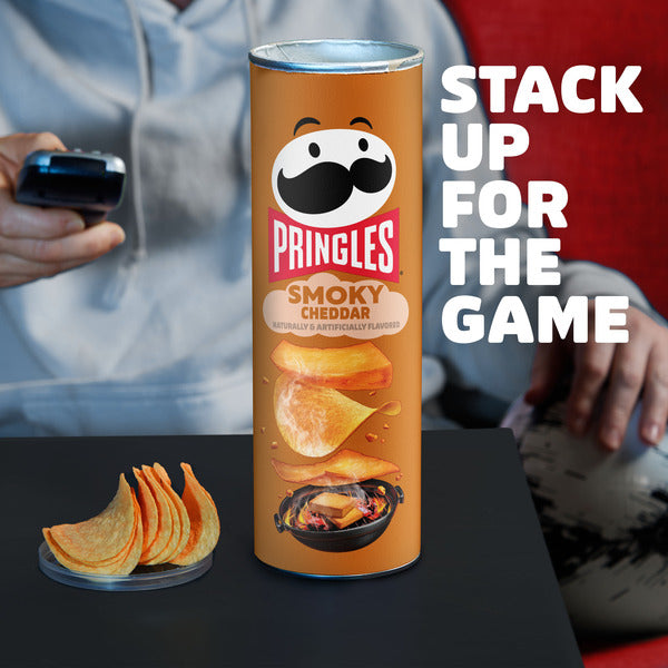 Pringles Smoky Cheddar can with chips on a table, people in the background