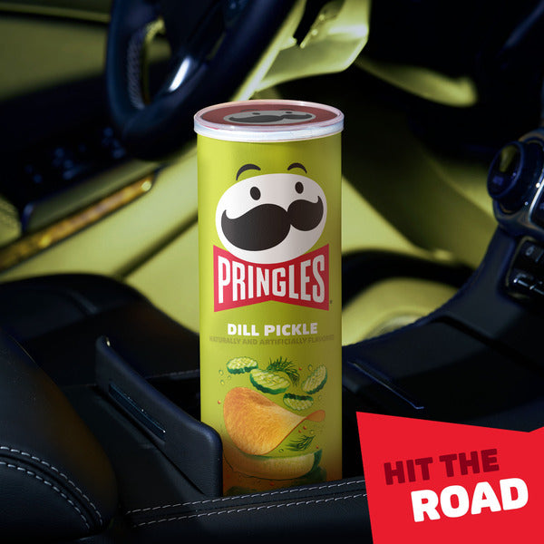 Pringles Dill Pickle chip can in a car cup holder with 'Hit the Road' text.