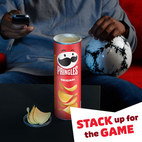 Pringles can with chips on a table, person sitting on a couch with a remote control, and text 'Stack up for the Game' on a red background.