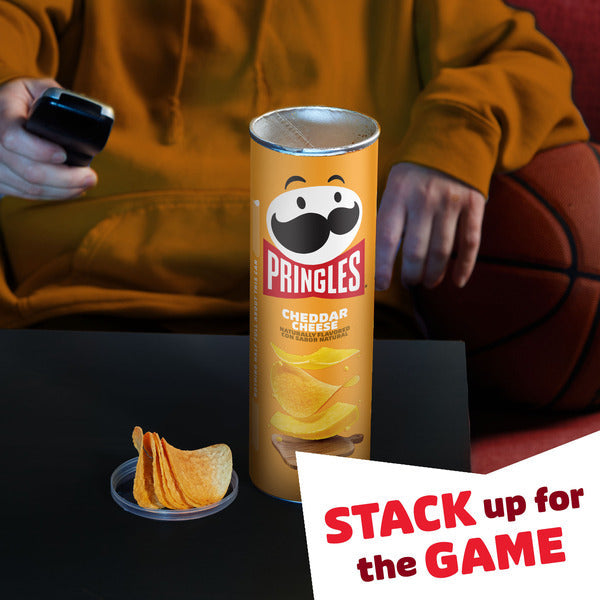 Pringles can of Cheddar Cheese flavor with a person sitting on a couch in the background.