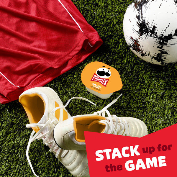 Soccer shoes, red shorts, soccer ball, and Pringles snack container on grass with 'Stack up for the Game' text.