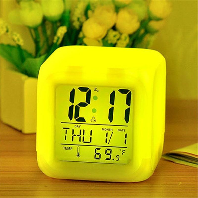 Yellow digital clock on a wooden surface with a blurred floral background