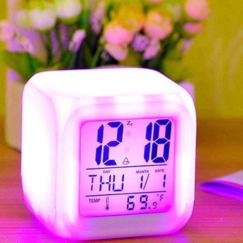 Digital clock with colorful LED display on a wooden surface with flowers in the background