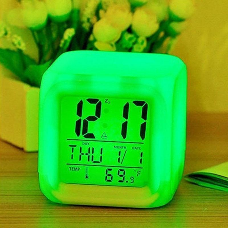 Green digital clock displaying time and date on a wooden surface with flowers in the background