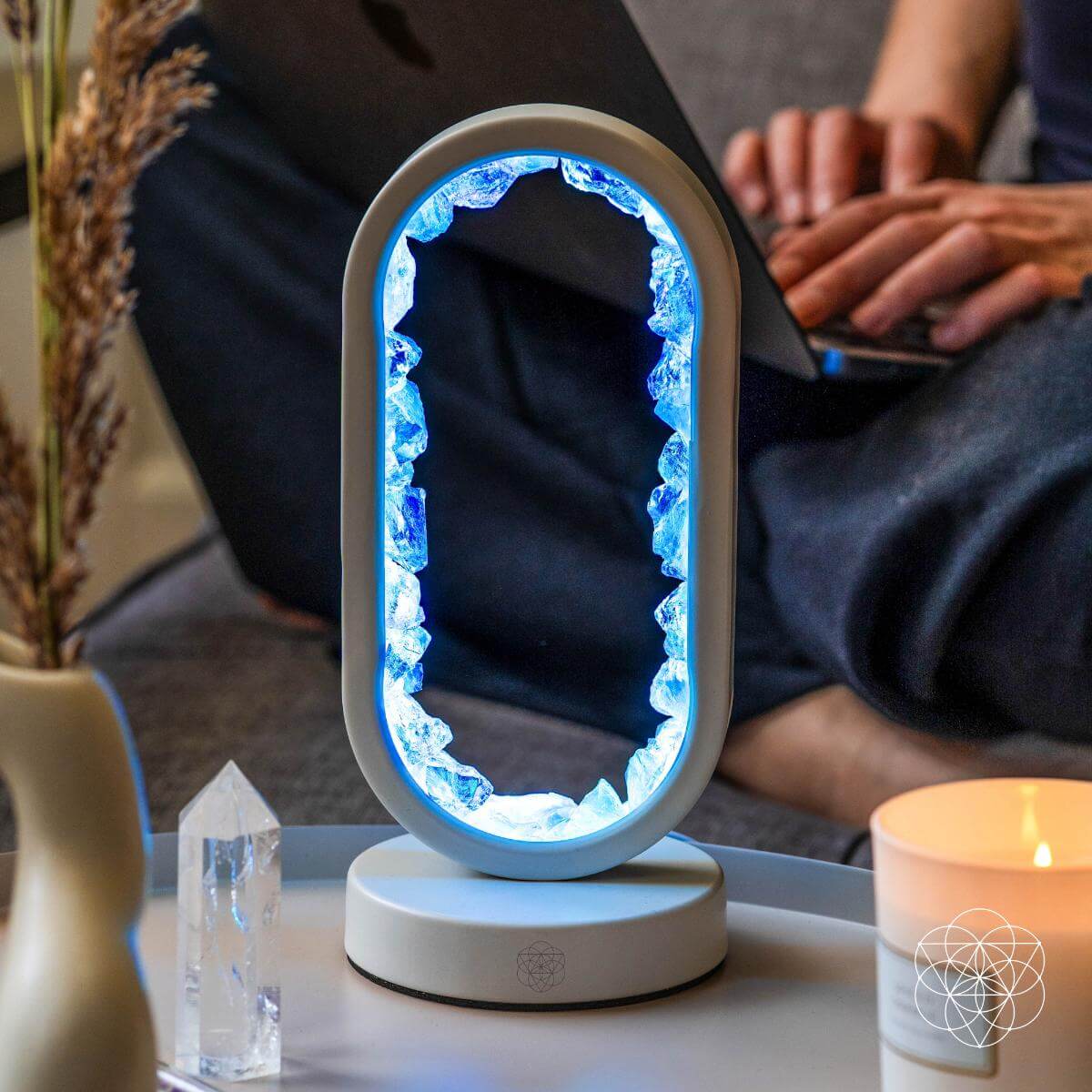 Decorative lamp with blue light on a table next to a person using a laptop. Manifest Success - Clear Quartz Lamp of Achievement