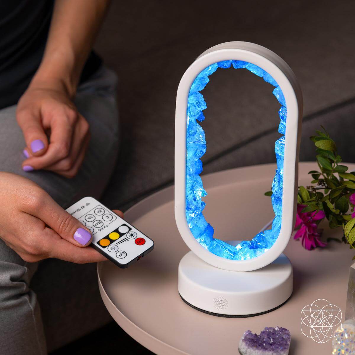 Person holding a remote control next to a glowing crystal-like lamp on a table. Manifest Success - Clear Quartz Lamp of Achievement