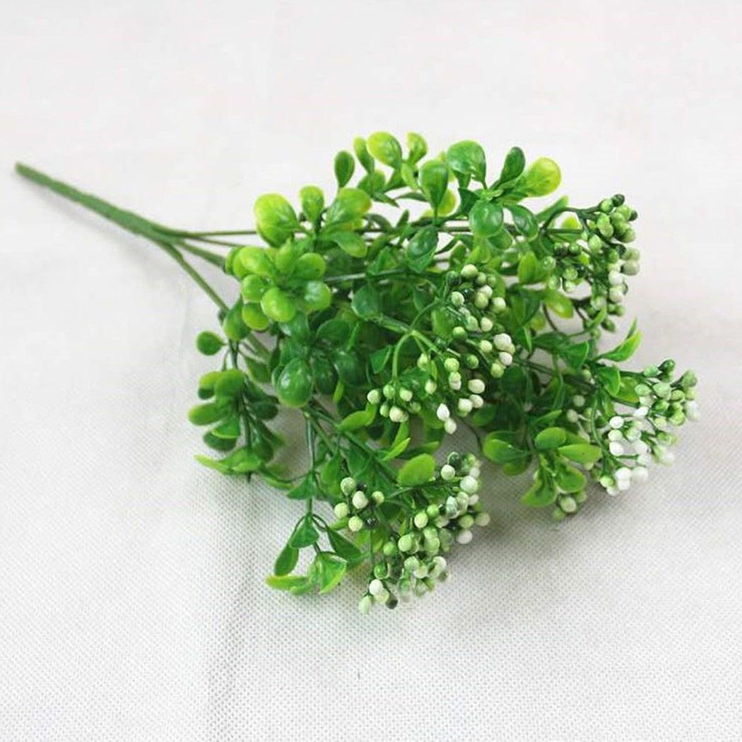 Artificial greenery with small white flowers on a light gray background