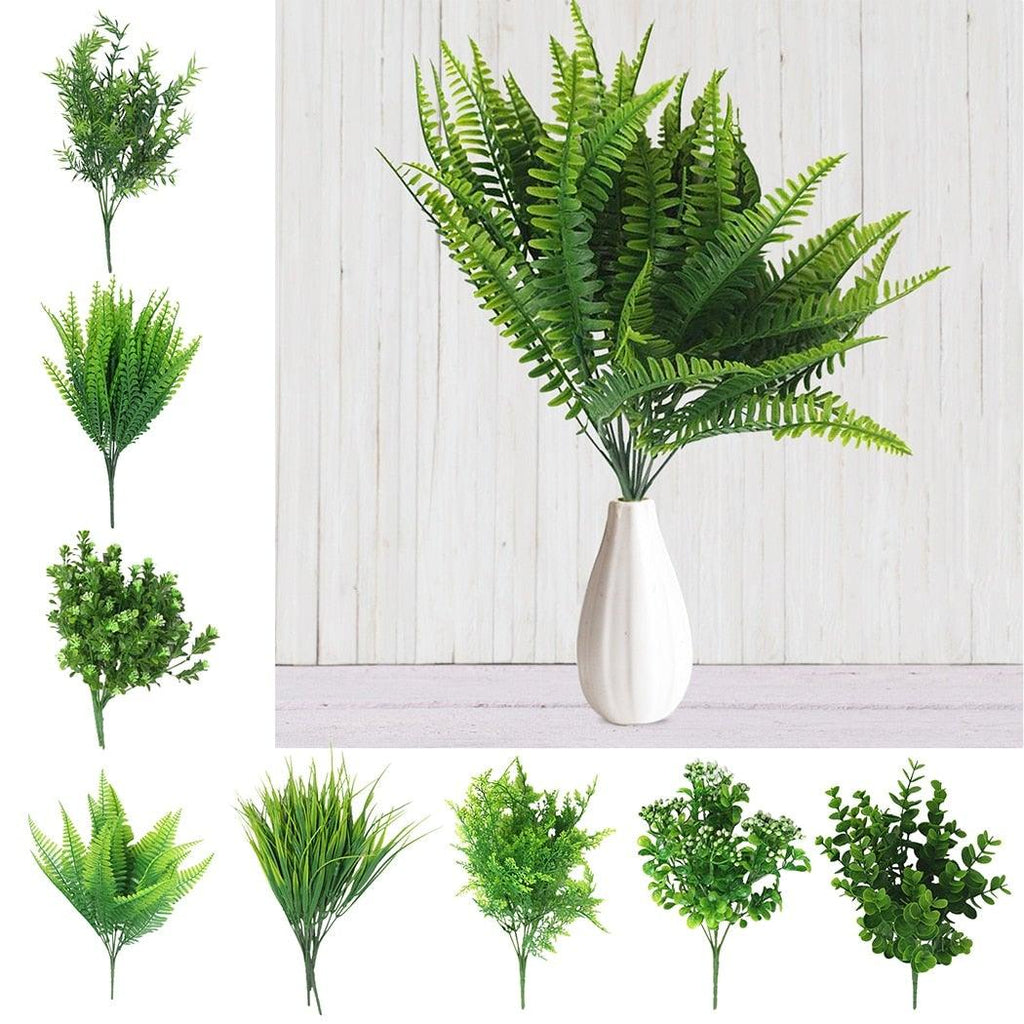 Collection of artificial green plants in vases against a white wooden panel background