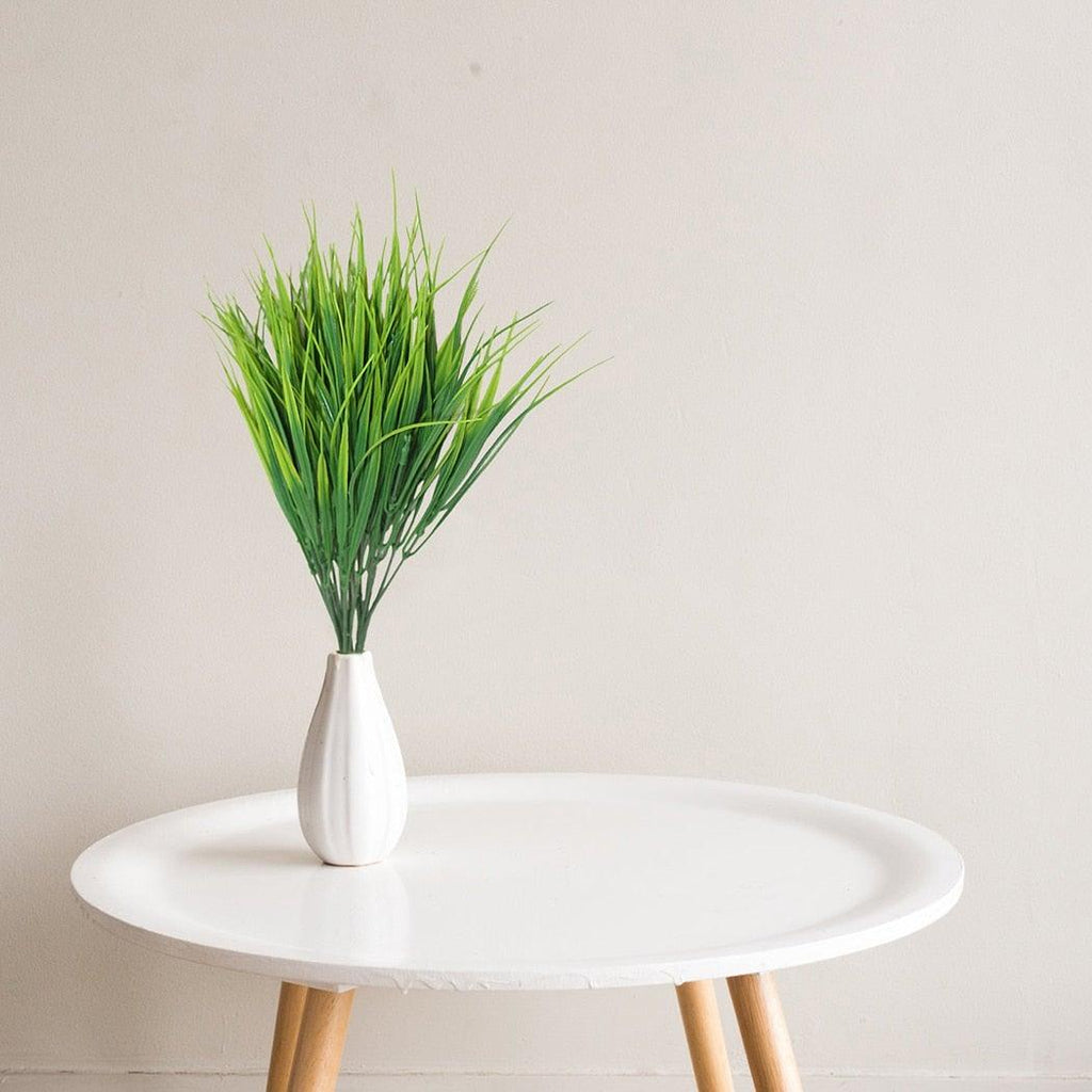 White vase with green grass on a round white table against a light gray background