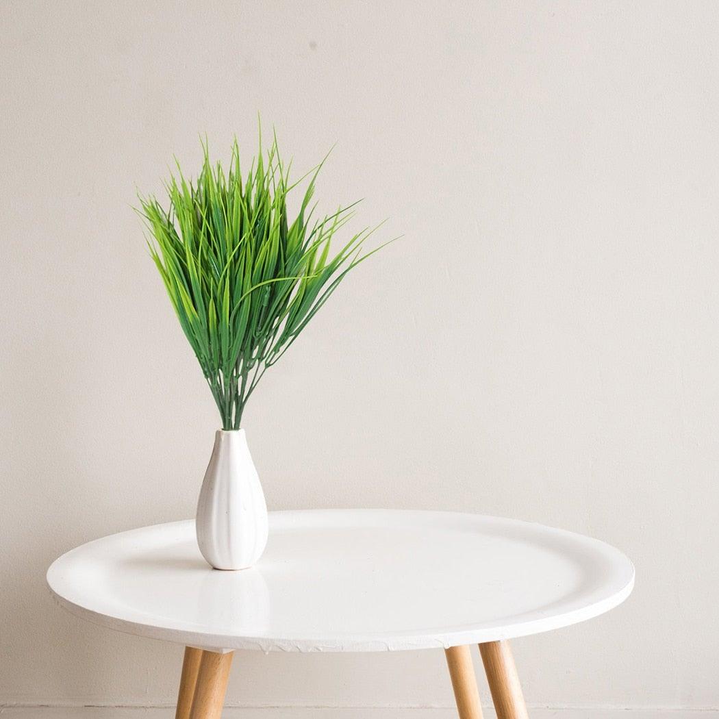 White vase with green grass on a round white table against a light gray background