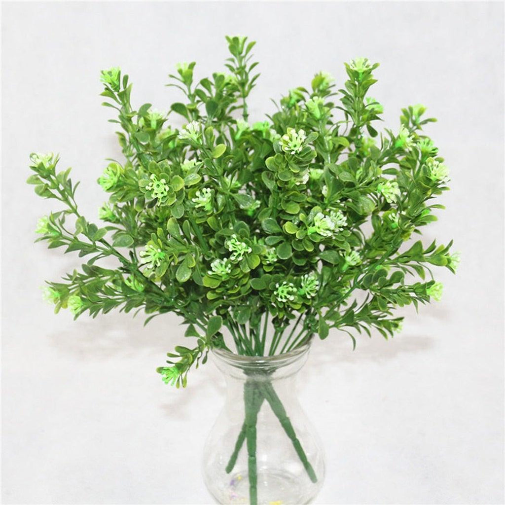 Artificial green plants in a clear glass vase on a light gray background