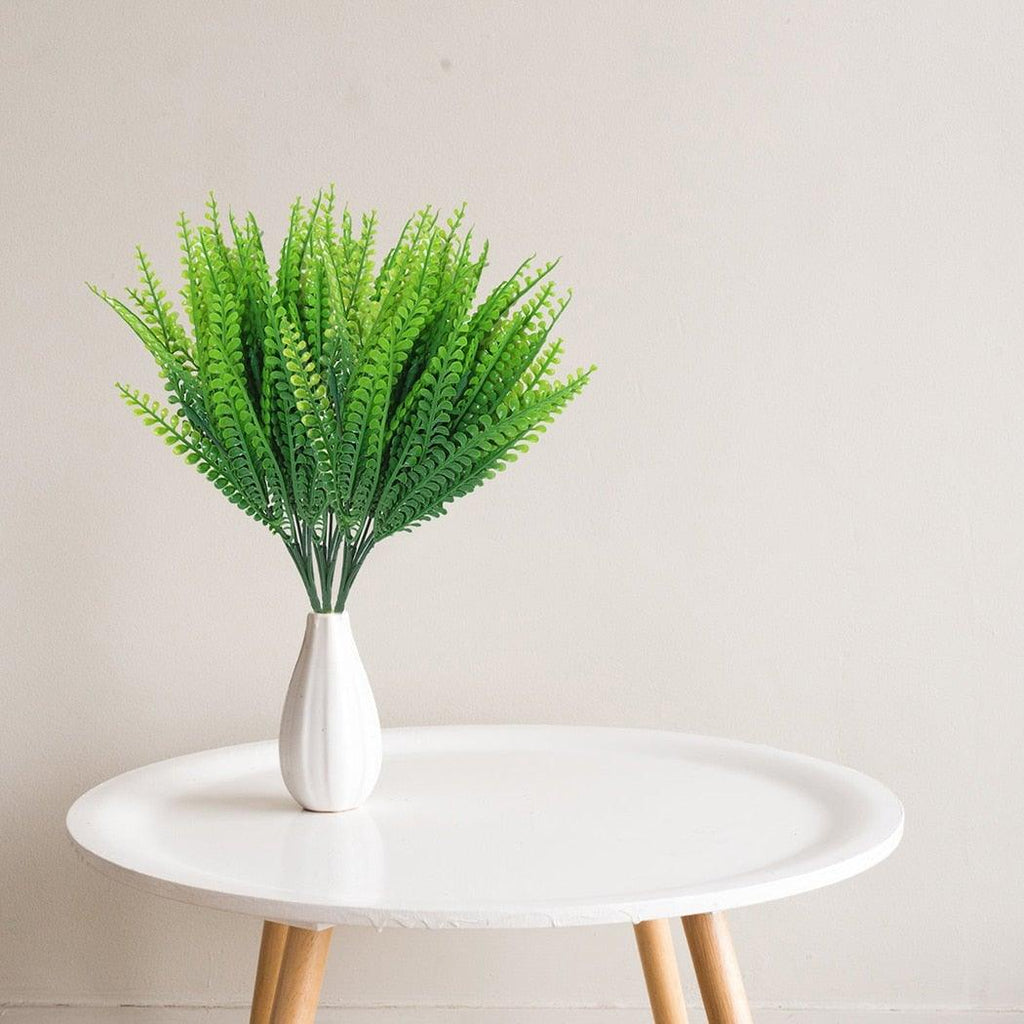 Green artificial plants in a white vase on a round white table with a beige background