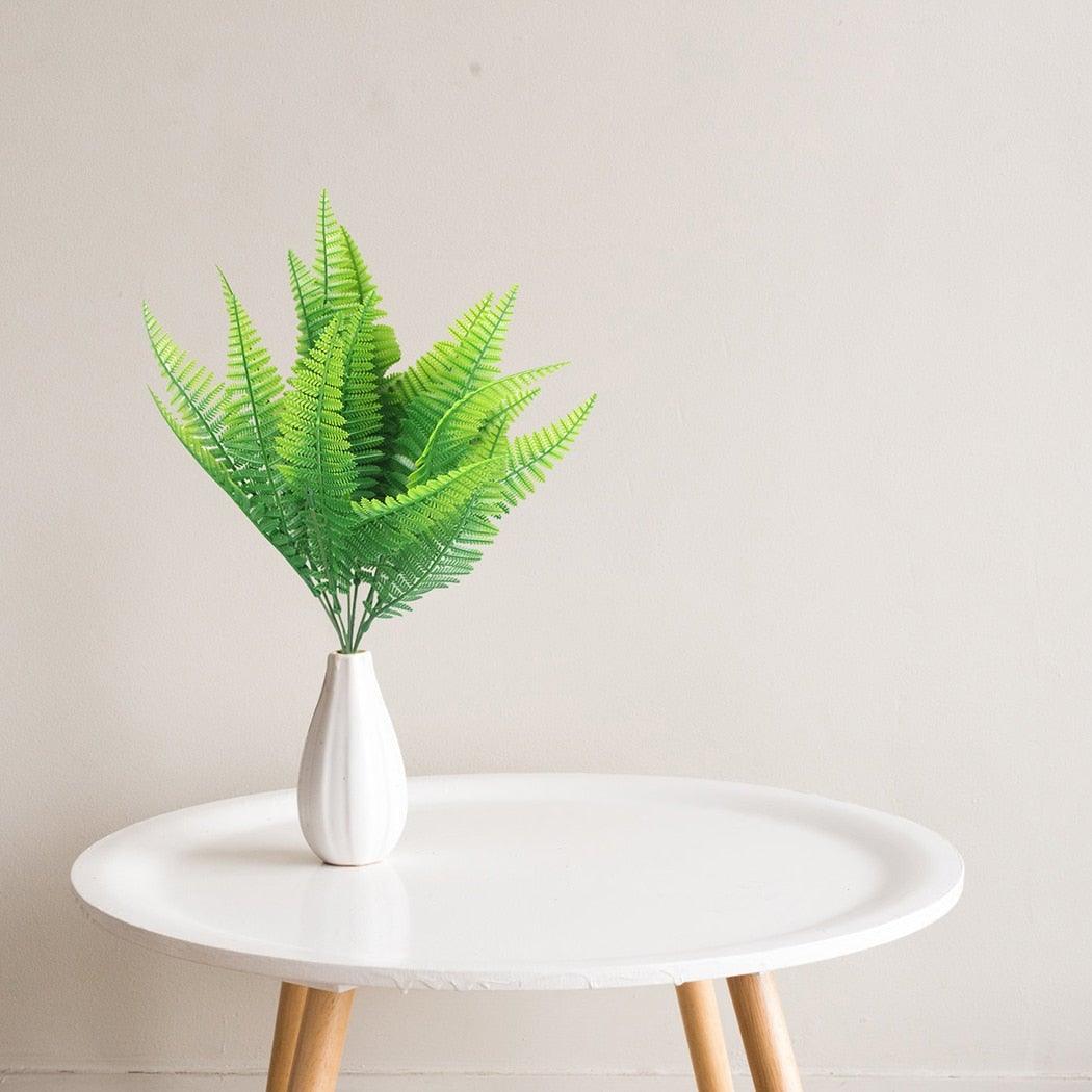 White vase with green ferns on a round white table against a light gray background
