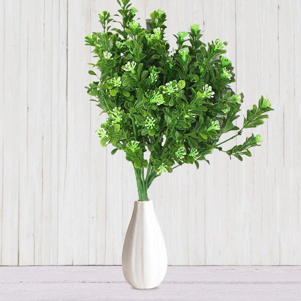 Green artificial plant in a white vase on a light wooden background