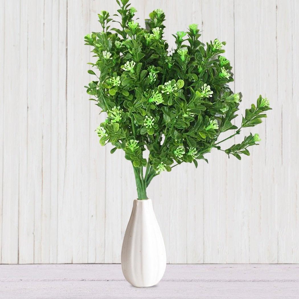 Green artificial plant in a white vase on a light wooden background