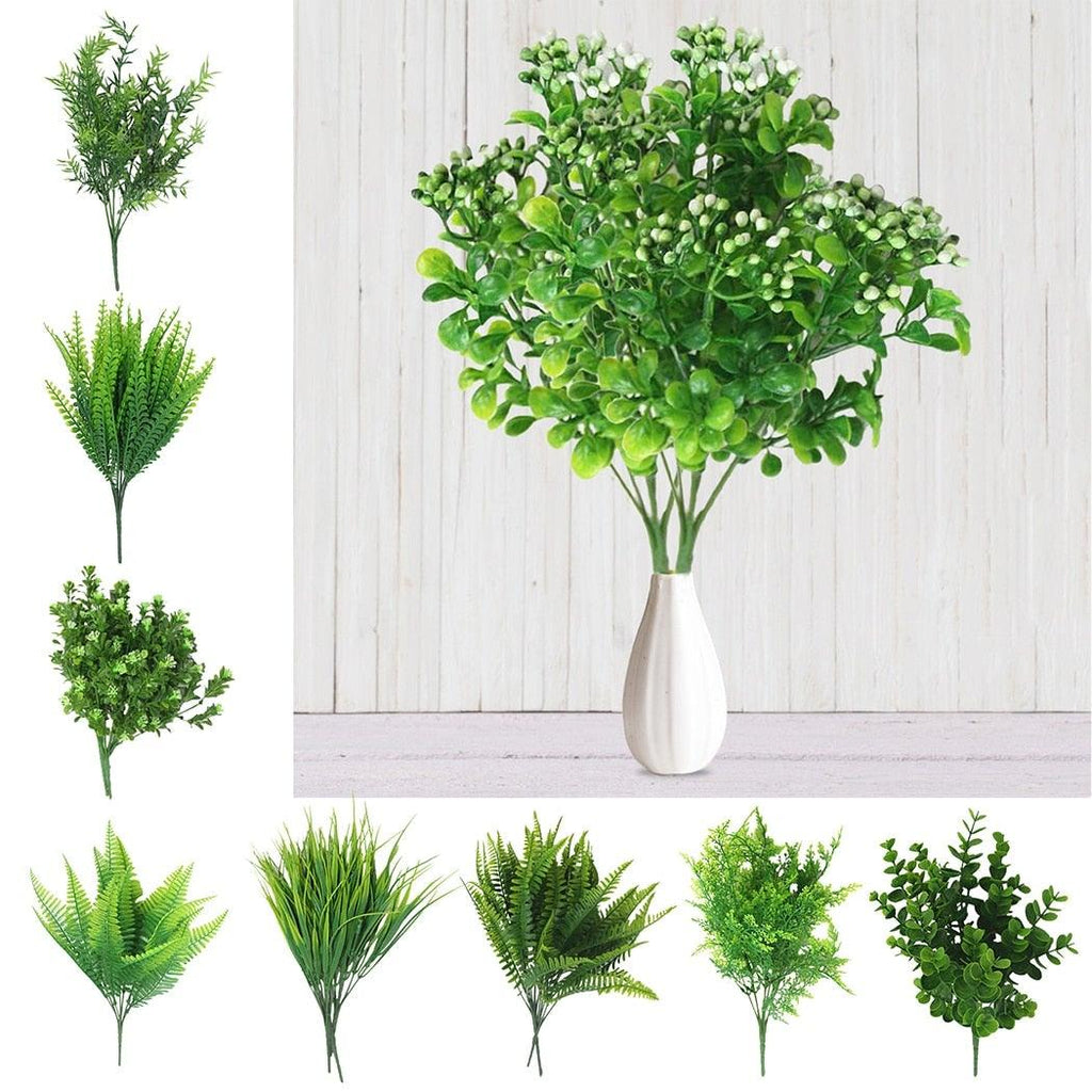 Collection of artificial green plants in vases against a white wooden panel background