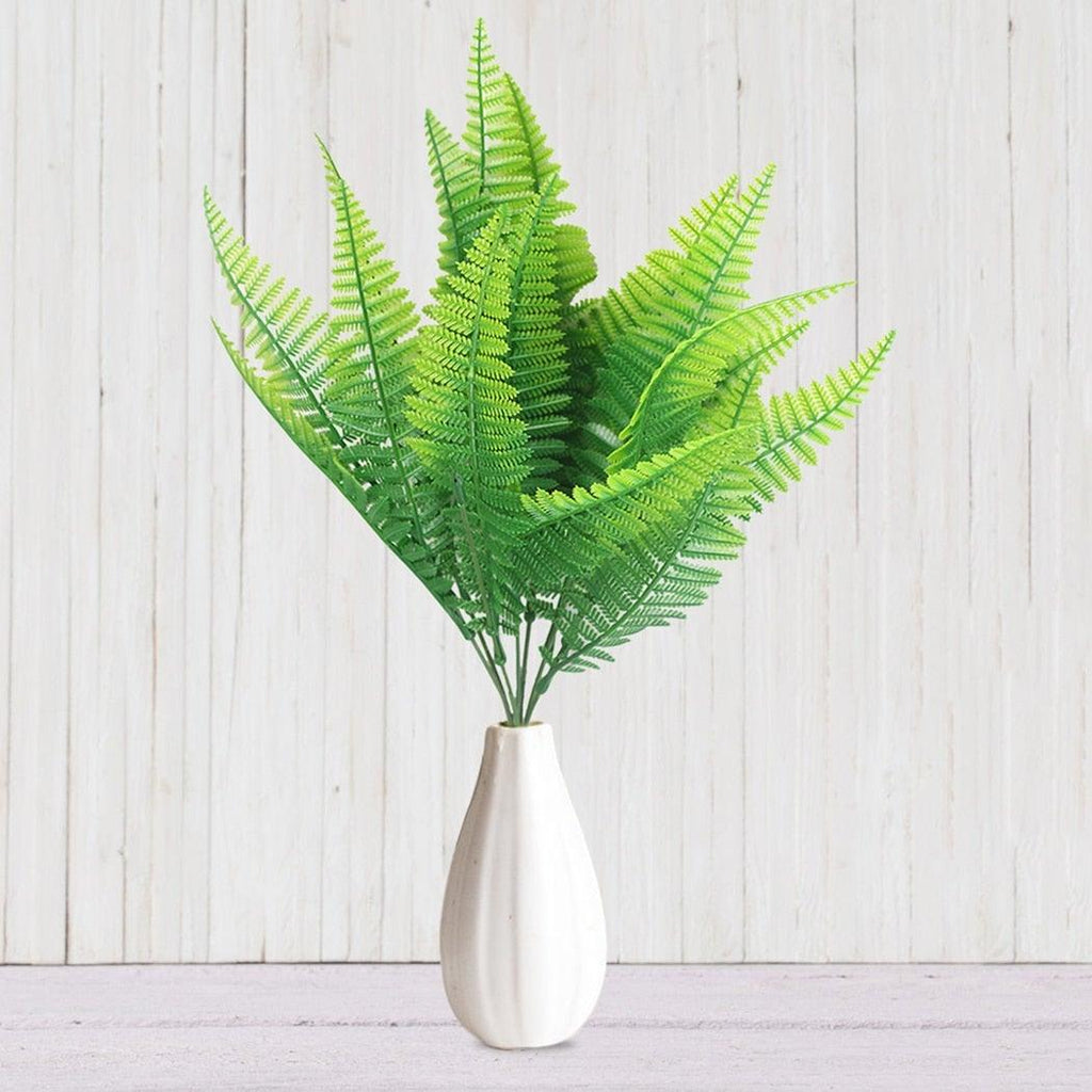 Green fern leaves in a white vase on a light wooden background