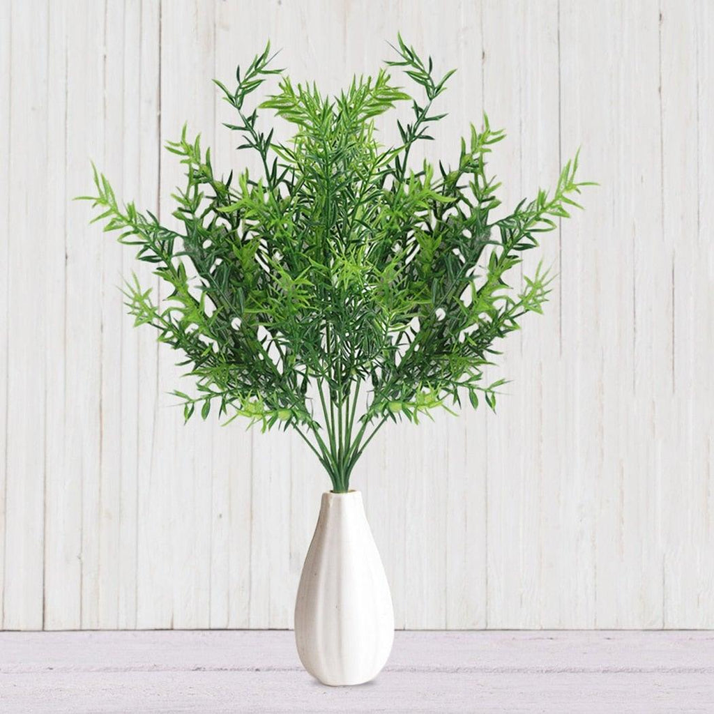 Green artificial plant in a silver vase on a light wooden background