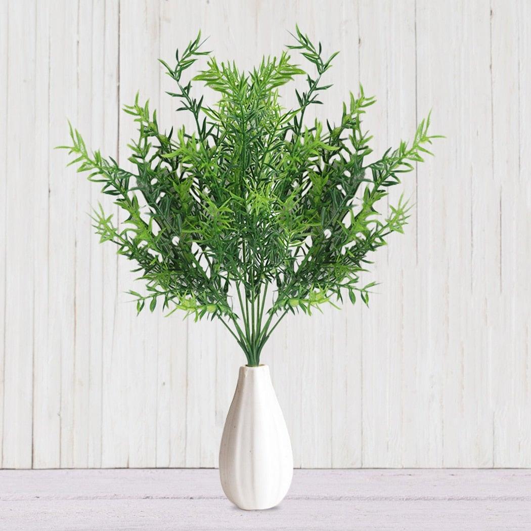 Green artificial plant in a silver vase on a light wooden background