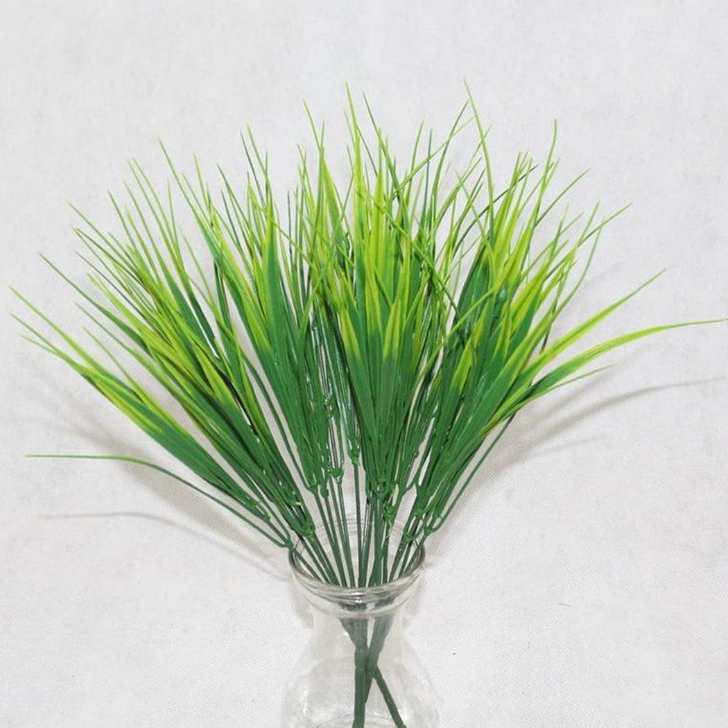 Artificial green grass in a clear glass vase on a white background