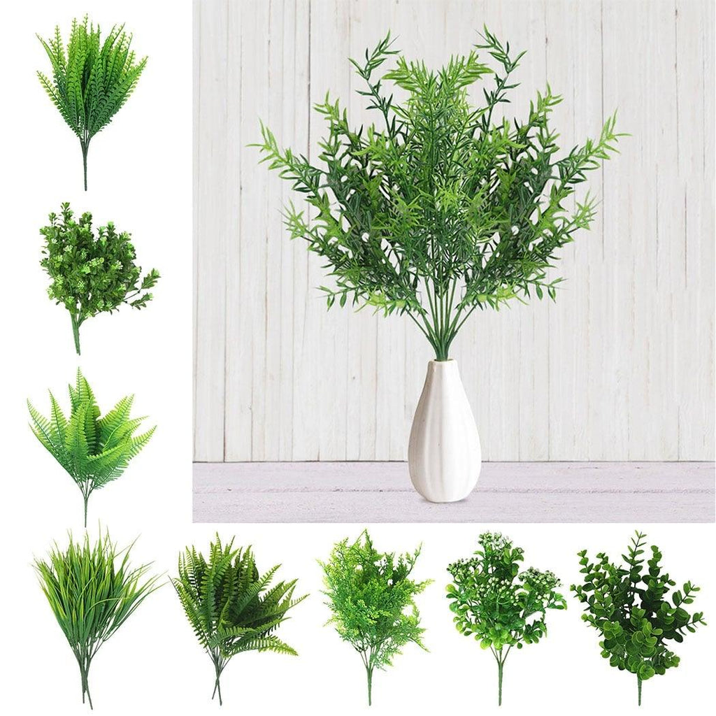 Set of artificial green plants in a white vase against a light wooden panel background