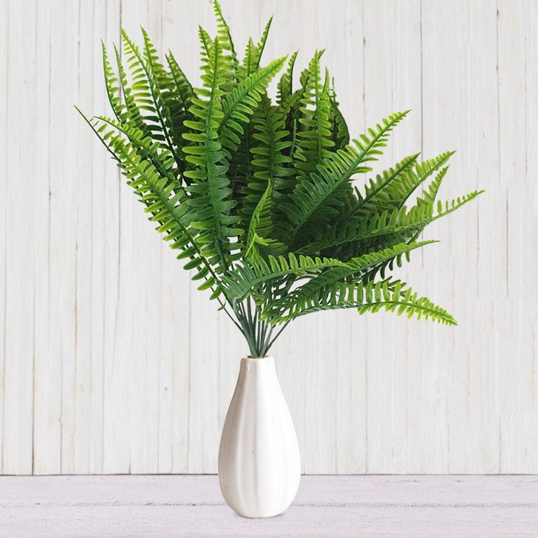 Artificial fern plant in a white vase on a light wooden background