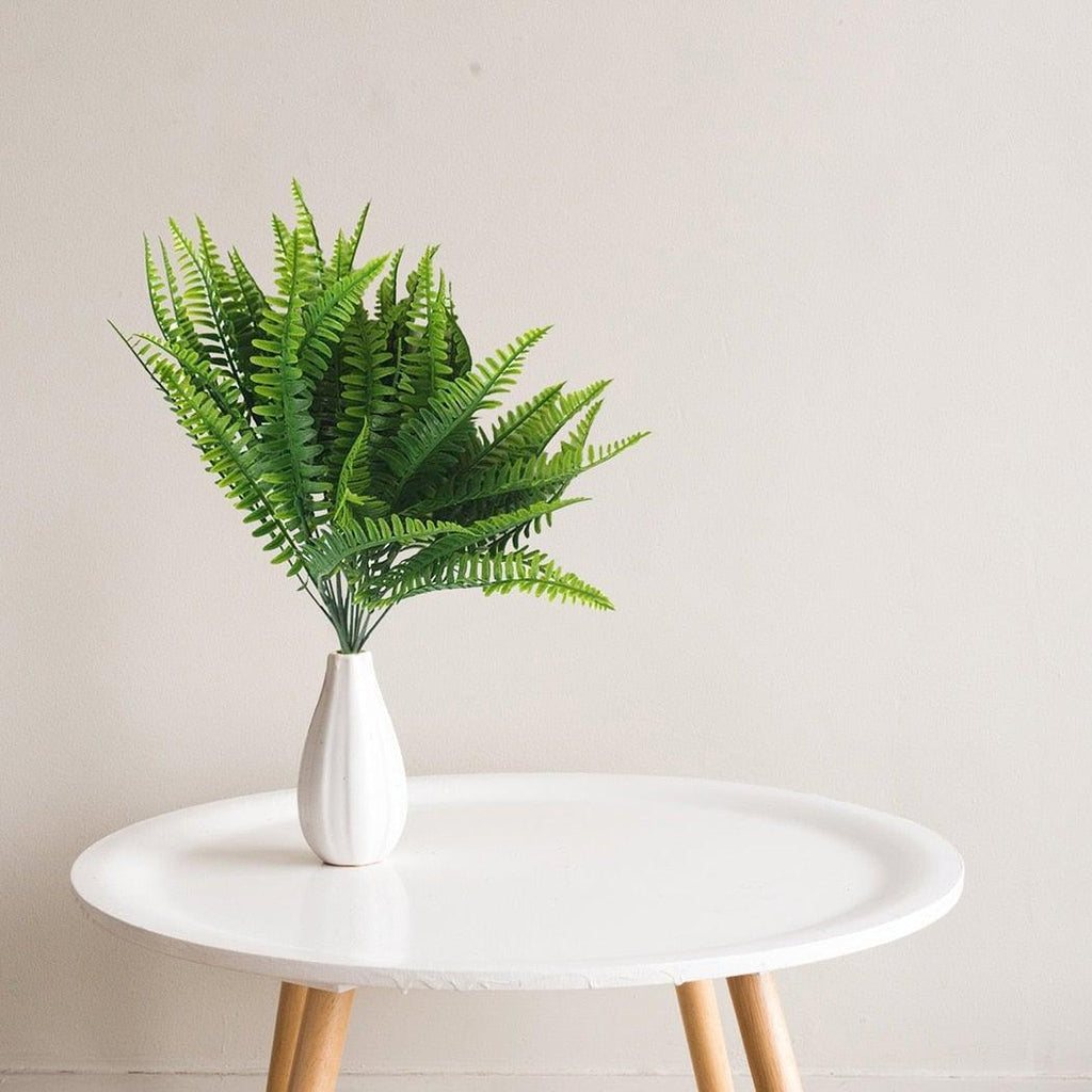 Fern plant in a white vase on a round white table against a beige wall