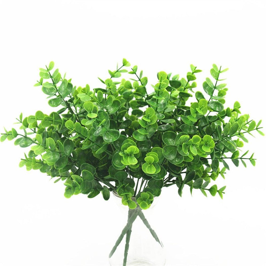 Artificial green leaves in a clear vase on a white background