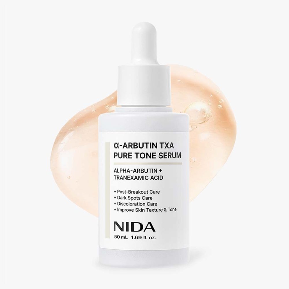 NIDA Alpha-Arbutin TXA Pure Tone Serum in a 50 ml white dropper bottle, set against a clean white background with a soft peach-colored cosmetic smear behind it.