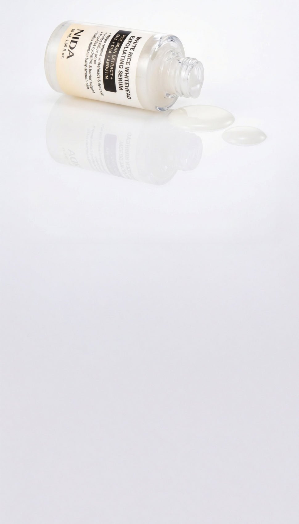 A clear glass bottle of NIPDA serum with a cream-colored label, lying on its side with a small amount of clear liquid spilled from the open top, set against a reflective white background.