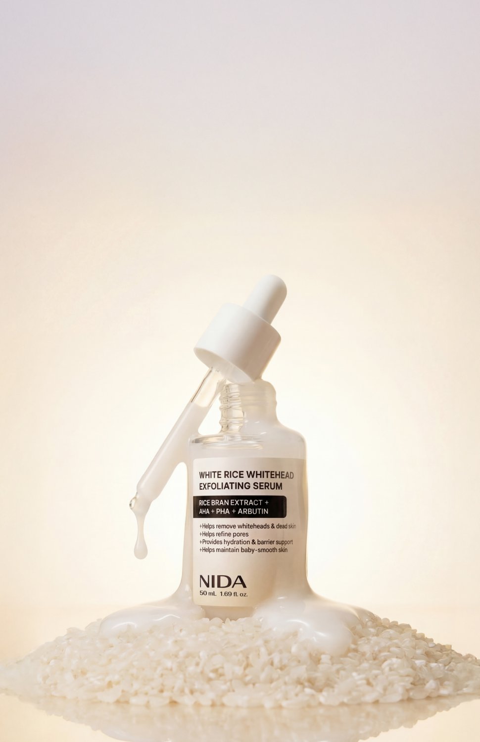NIDA White Rice Whitehead Exfoliating Serum in a frosted glass dropper bottle, styled with a dripping white serum and a bed of white rice grains on a reflective surface against a warm cream background.