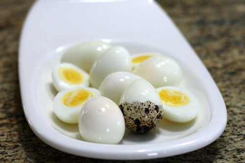 Hard-boiled organic jumbo quail eggs on a white serving dish, showcasing peeled whole and halved eggs with bright golden yolks, farm-fresh from Moses Lake, Washington.