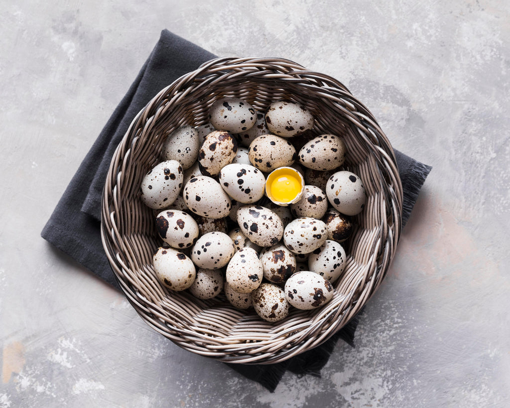 Basket of organic farm-fresh jumbo quail eggs with one cracked open to reveal a vibrant golden yolk, hand-packed in Moses Lake, Washington, rich in protein and perfect for healthy cooking, gourmet recipes, pickling, and nutritious snacks.