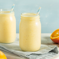 Creamy orange creamsicle smoothie served in two mason jars with striped paper straws, fresh orange slices, and a soft blue background, perfect for a refreshing citrus breakfast or healthy snack