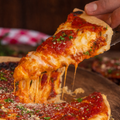Slice of pizza being lifted with stringy cheese, wooden table in the background