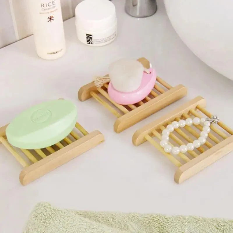 Three wooden soap dishes with soap and beads on a bathroom counter.