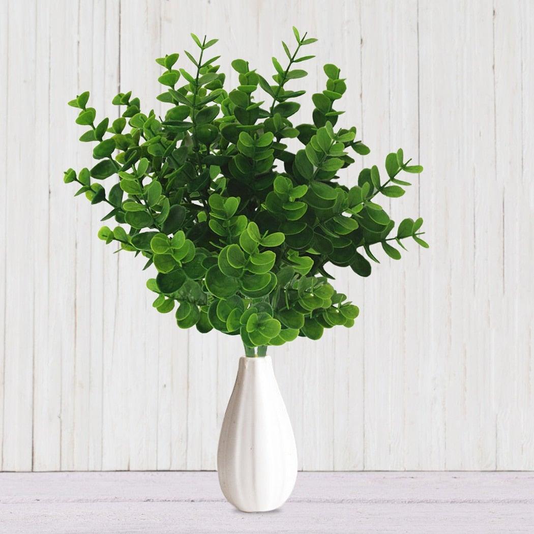 Green artificial plant in a white vase on a light wooden background