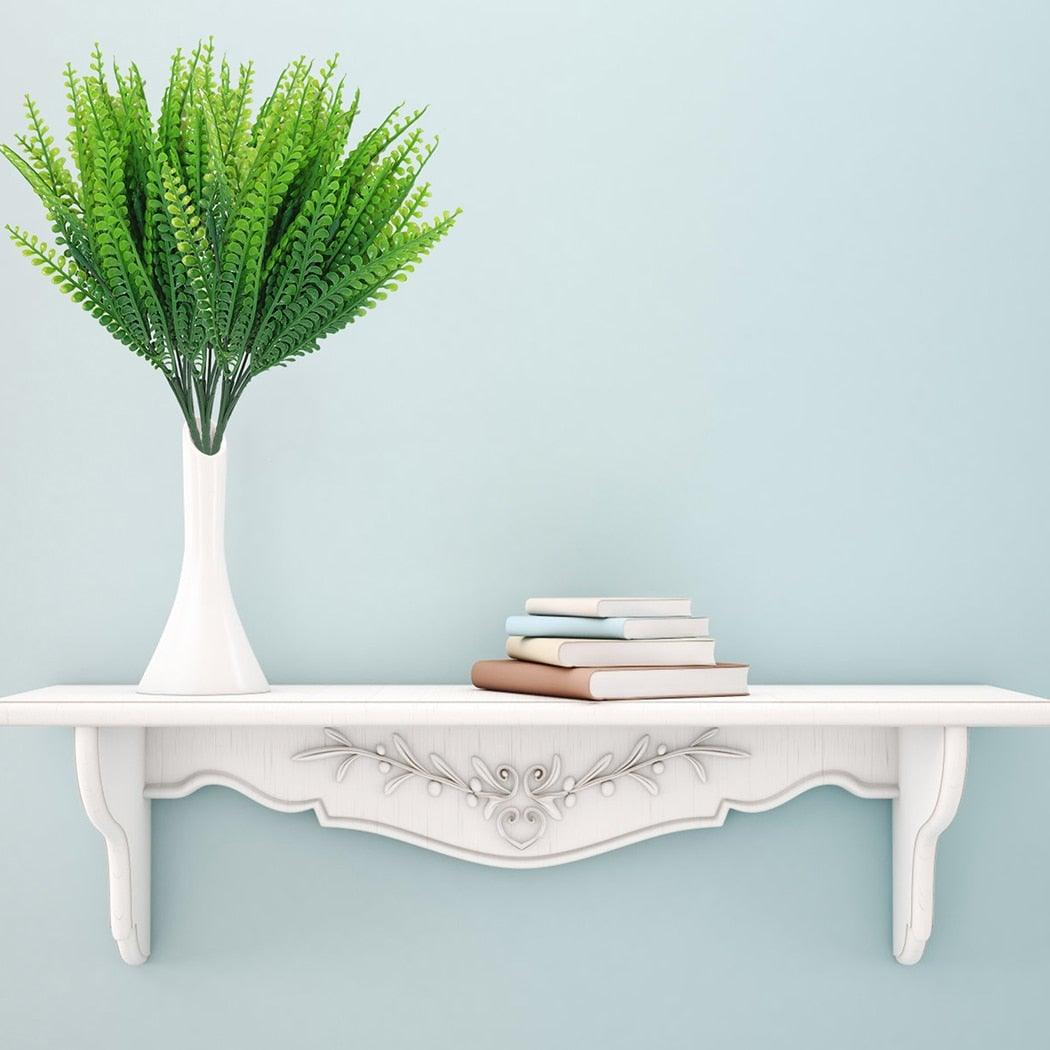 White table with a vase of green plants and books against a light blue wall