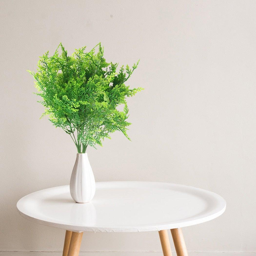 White vase with greenery on a round white table against a light background