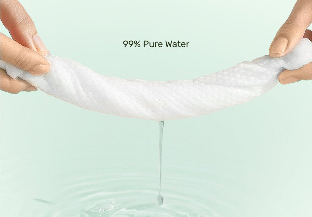 Hands stretching a thick, ultra-soft white baby wipe as pure water drips into a pool below, highlighting the wipe's 99% pure water formula on a soft light green background.