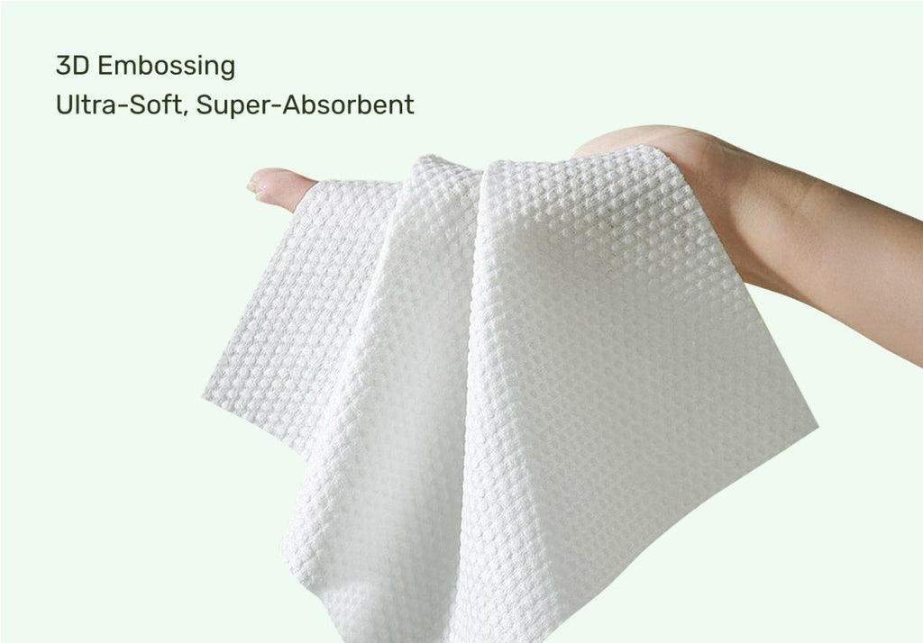 Hand holding a thick, ultra-soft white embossed baby wipe, showcasing the 3D textured design and super-absorbent, premium plant-based material against a light green background with text highlighting its ultra-soft and super-absorbent features.