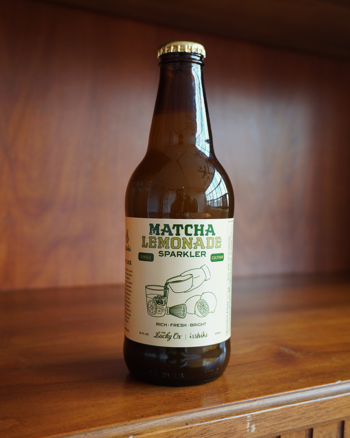 Bottle of matcha lemonade sparkler on a wooden surface with a blurred background