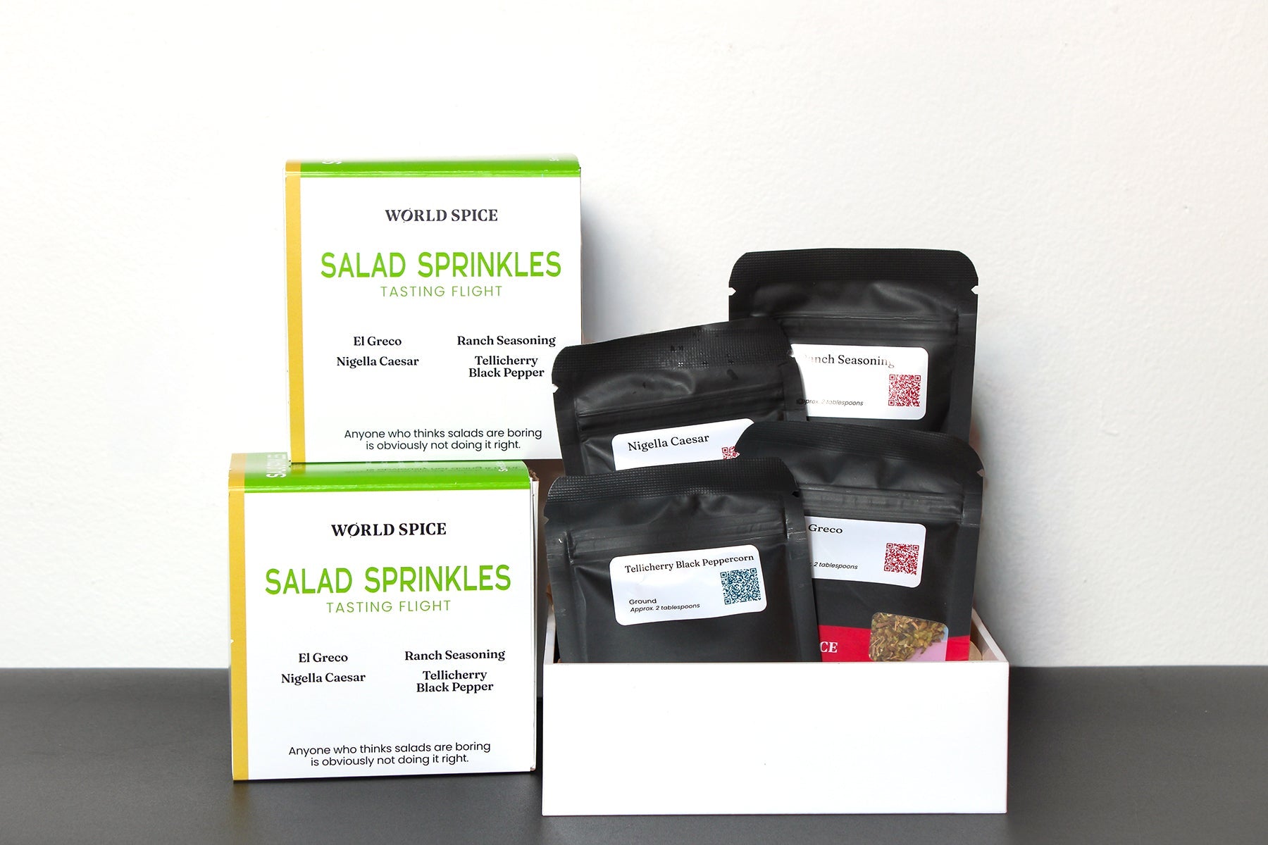 World Spice Salad Sprinkles Tasting Flight gift set featuring four gourmet seasoning blends, including Greek, Ranch, Nigella Caesar, and Tellicherry Black Pepper, with artisan spice pouches displayed in a white tasting tray and retail boxes on a clean white background.