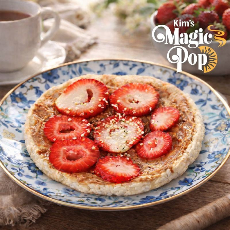 Kim's Magic Pop rice cake topped with creamy spread and fresh sliced strawberries on a decorative blue floral plate, served with coffee in a cozy breakfast setting.