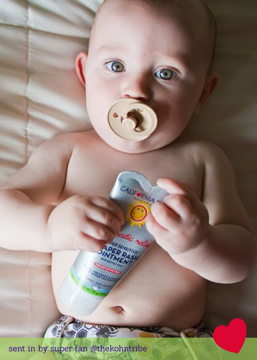 Baby holding a tube of Calendula Baby Rash Ointment with a pacifier in mouth. California Baby® (No Fragrance) Super Sensitive™ Diaper Rash Ointment