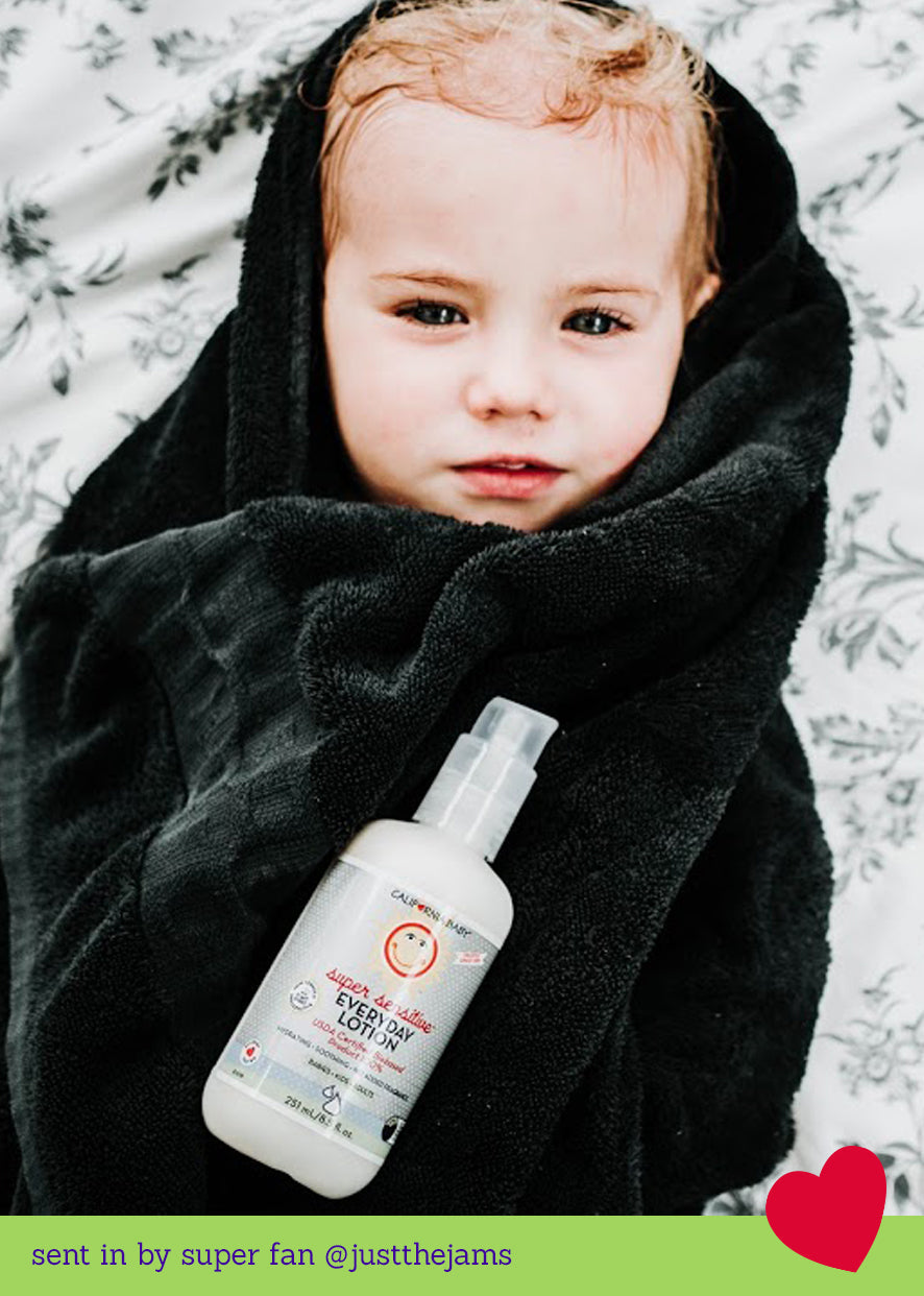 Child wrapped in a black blanket with a bottle of lotion on a snowy background California Baby® (No Fragrance) Super Sensitive™ Everyday Lotion