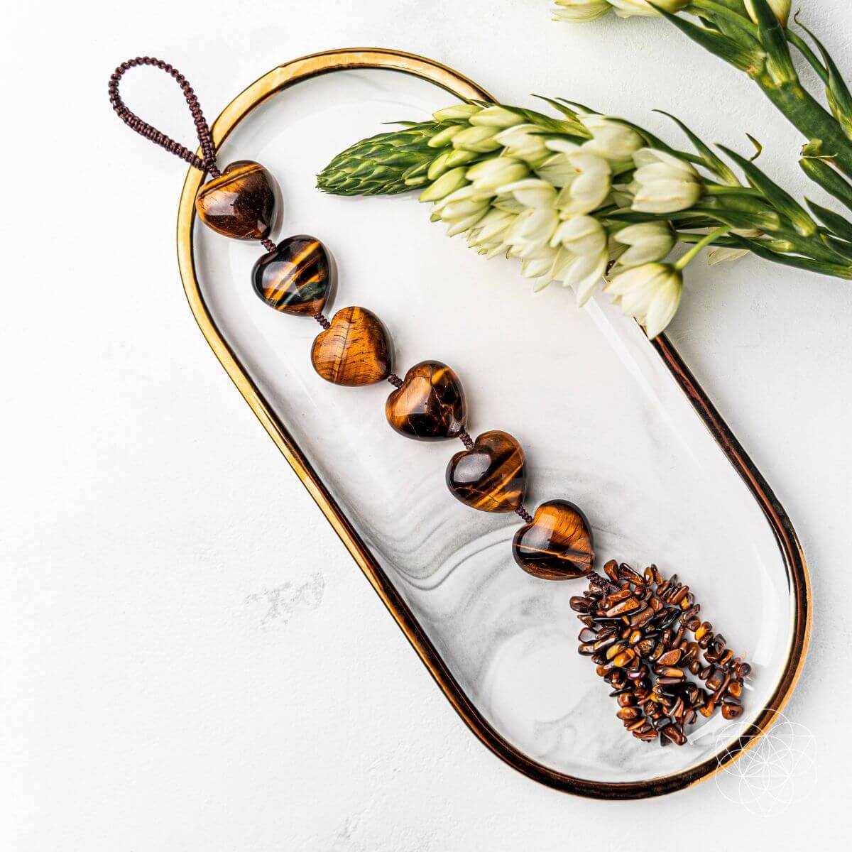 Tortoiseshell beaded necklace on a marble tray with white flowers and green leaves. Protection Tassel with Tiger's Eye Crystal for Protection, Positive Energy & Car Charm