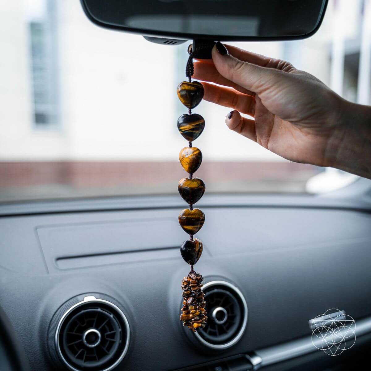 Hand holding a beaded car hanging charm in front of a car's rearview mirror. Protection Tassel with Tiger's Eye Crystal for Protection, Positive Energy & Car Charm